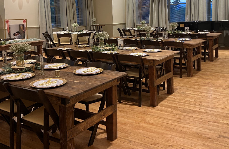 Wedding reception with wooden tables and chairs set for a luncheon, with flower arrangements