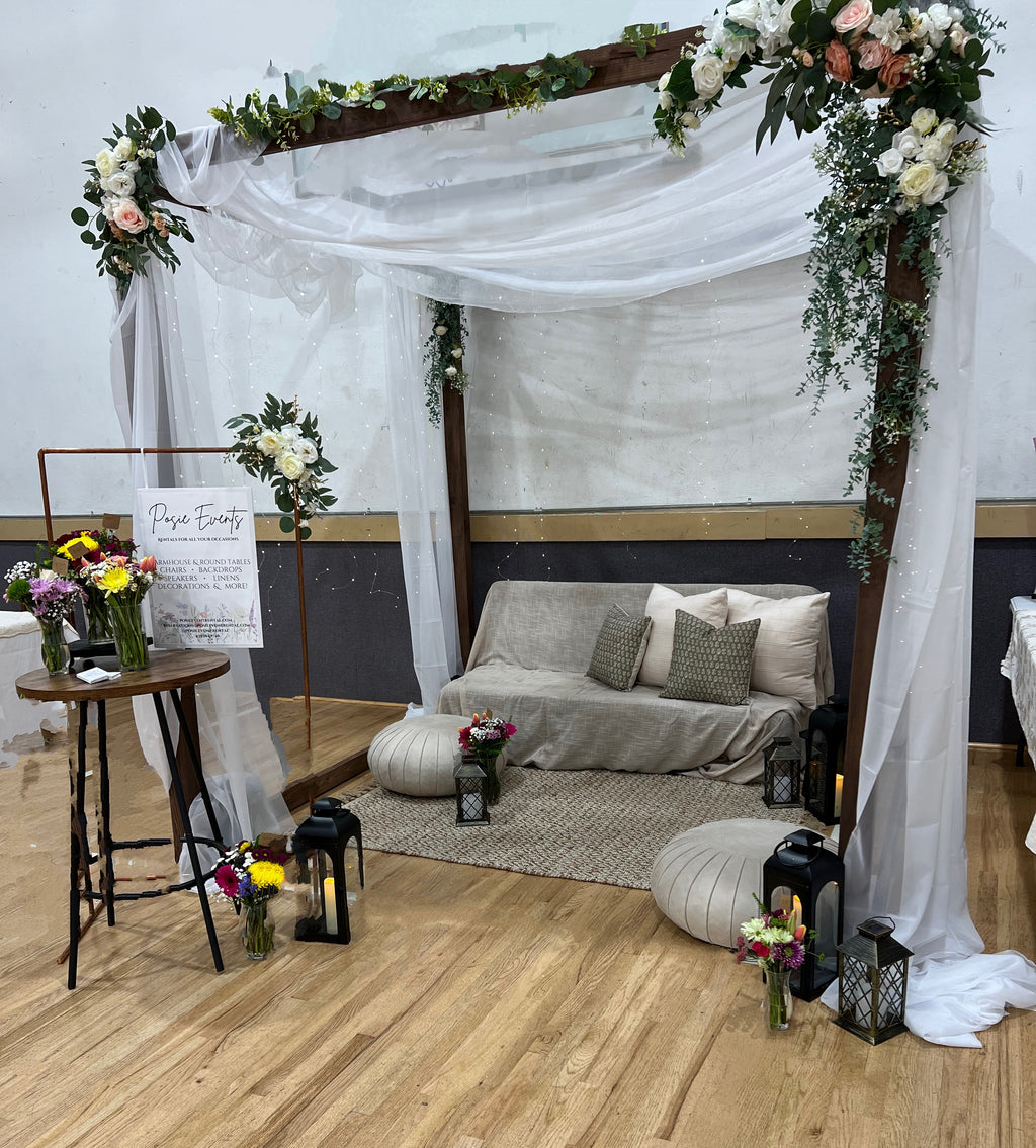 Decorative setup with a canopy, flowers, and a couch in a room.