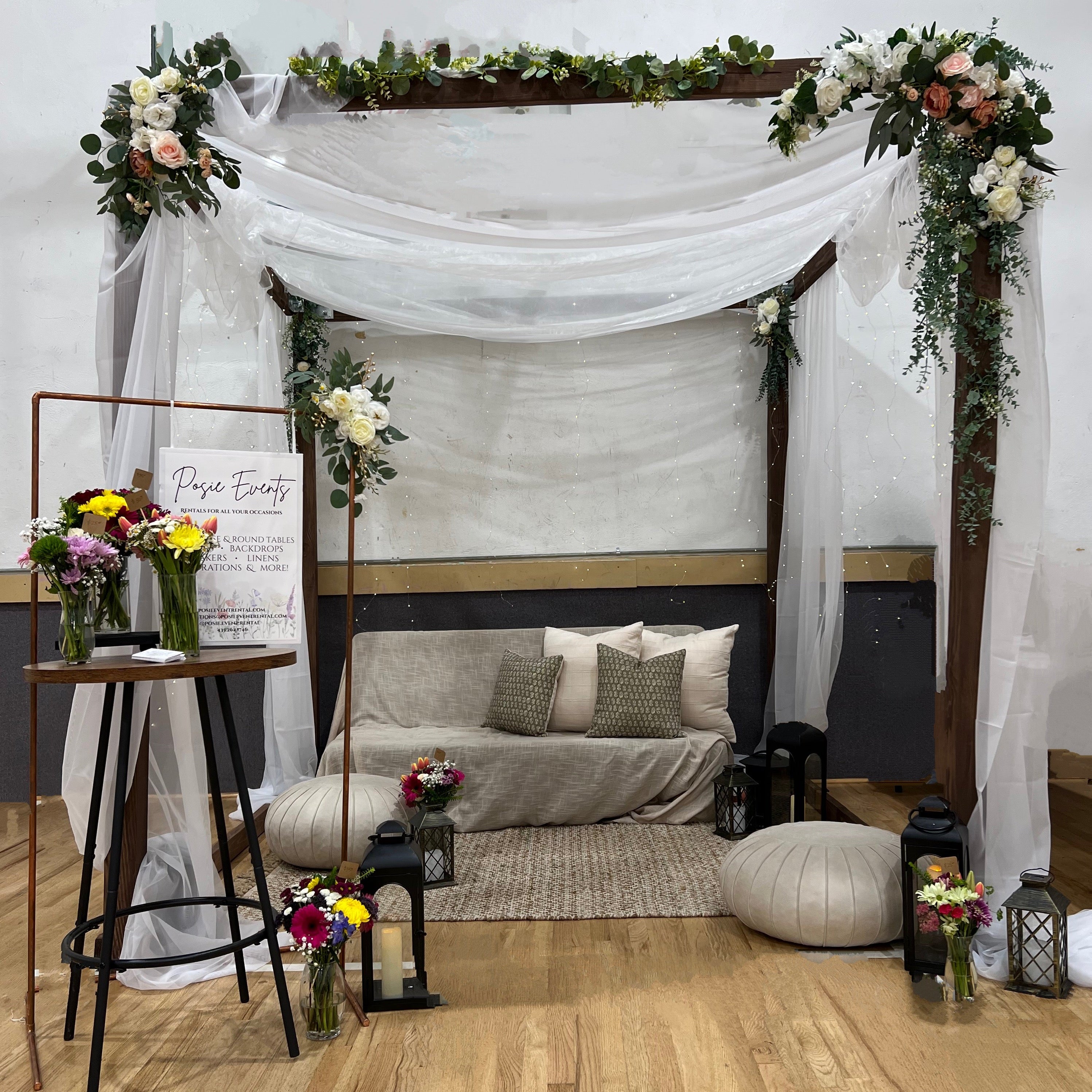 Decorative setup with a canopy, flowers, and a couch in a room.