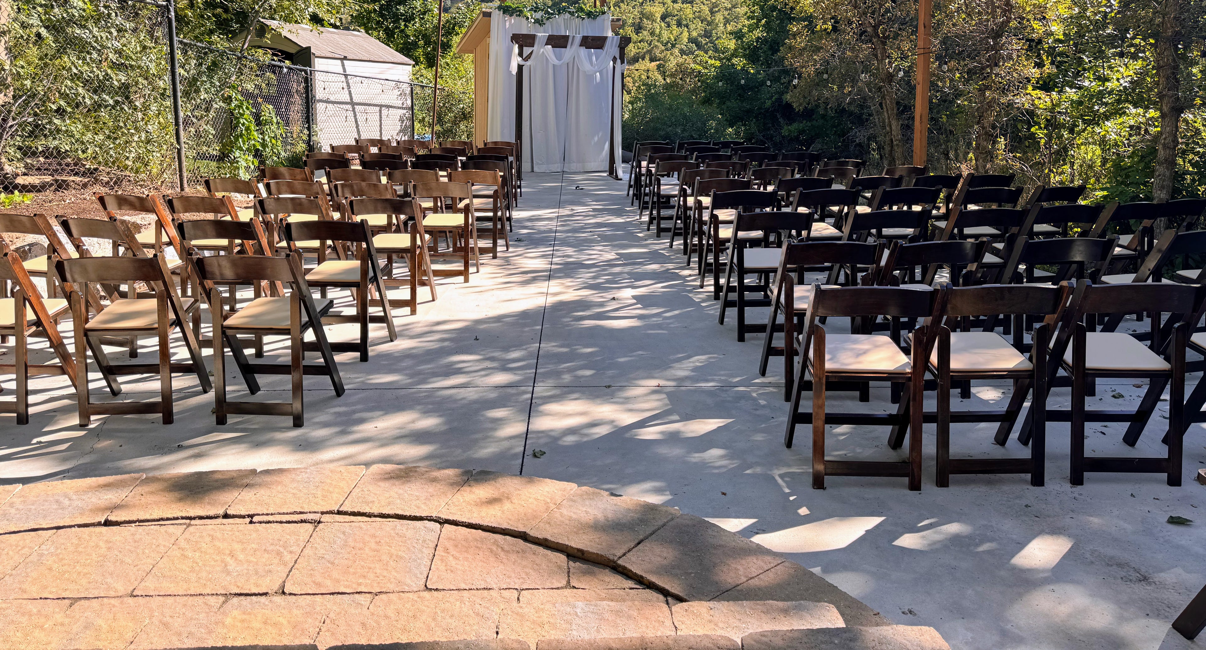 Outdoor wedding setup with rows of chairs on a concrete path.
