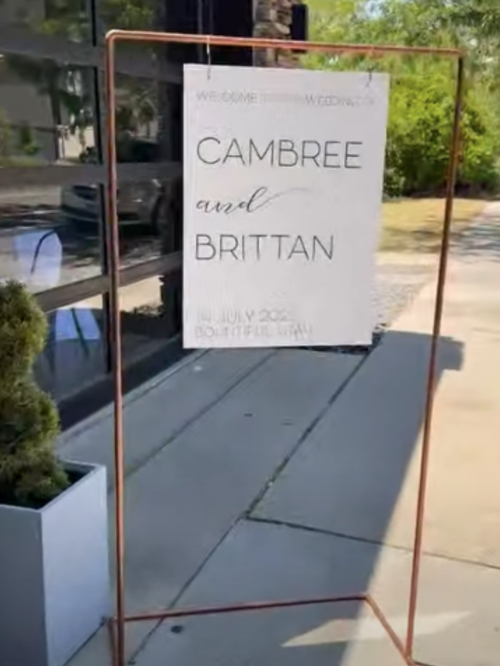 Wedding sign with 'Cambree and Brittan' on a stand outdoors.