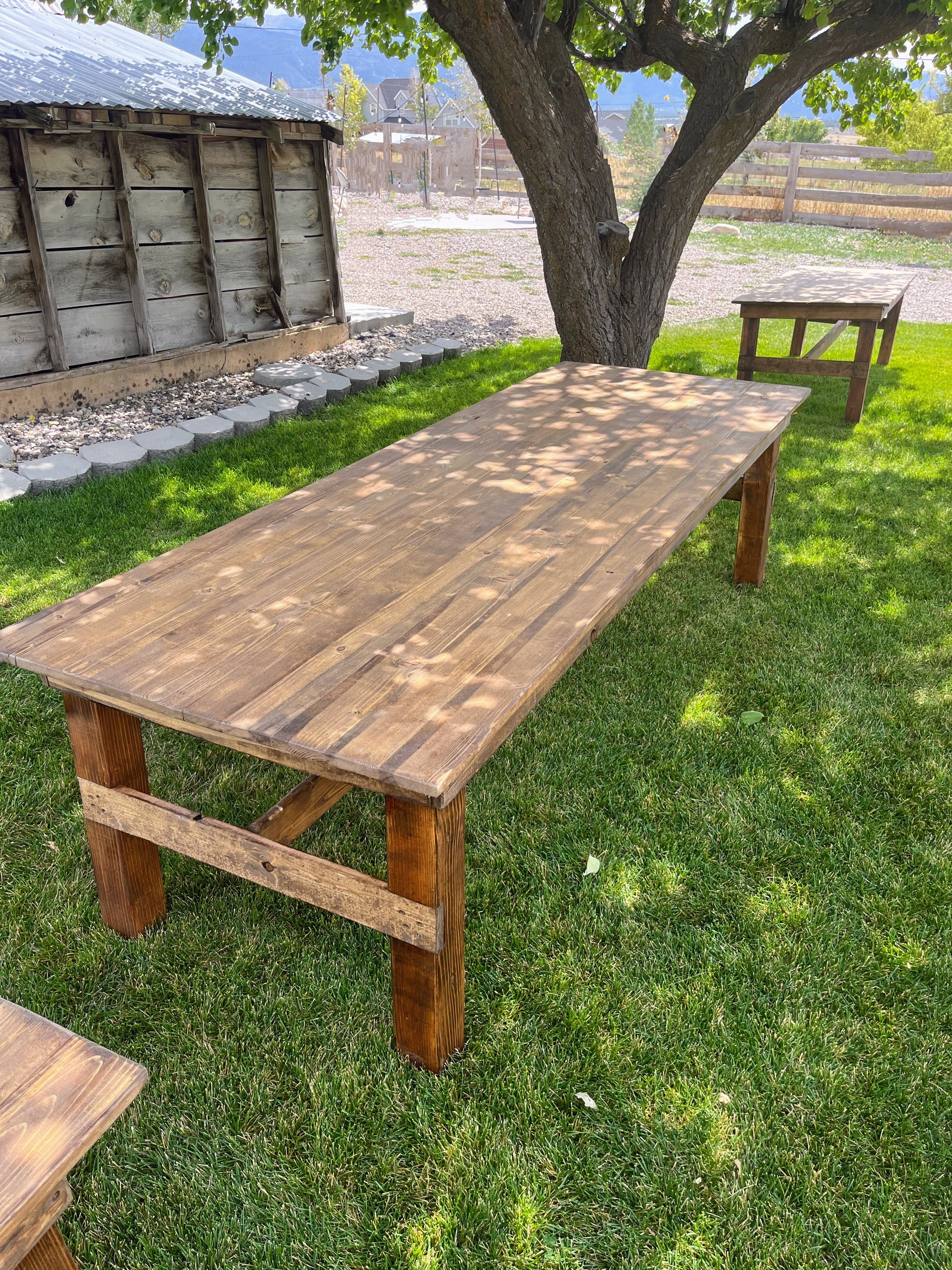 Wooden table outdoors on a grassy area with a rustic building and tree in the background.