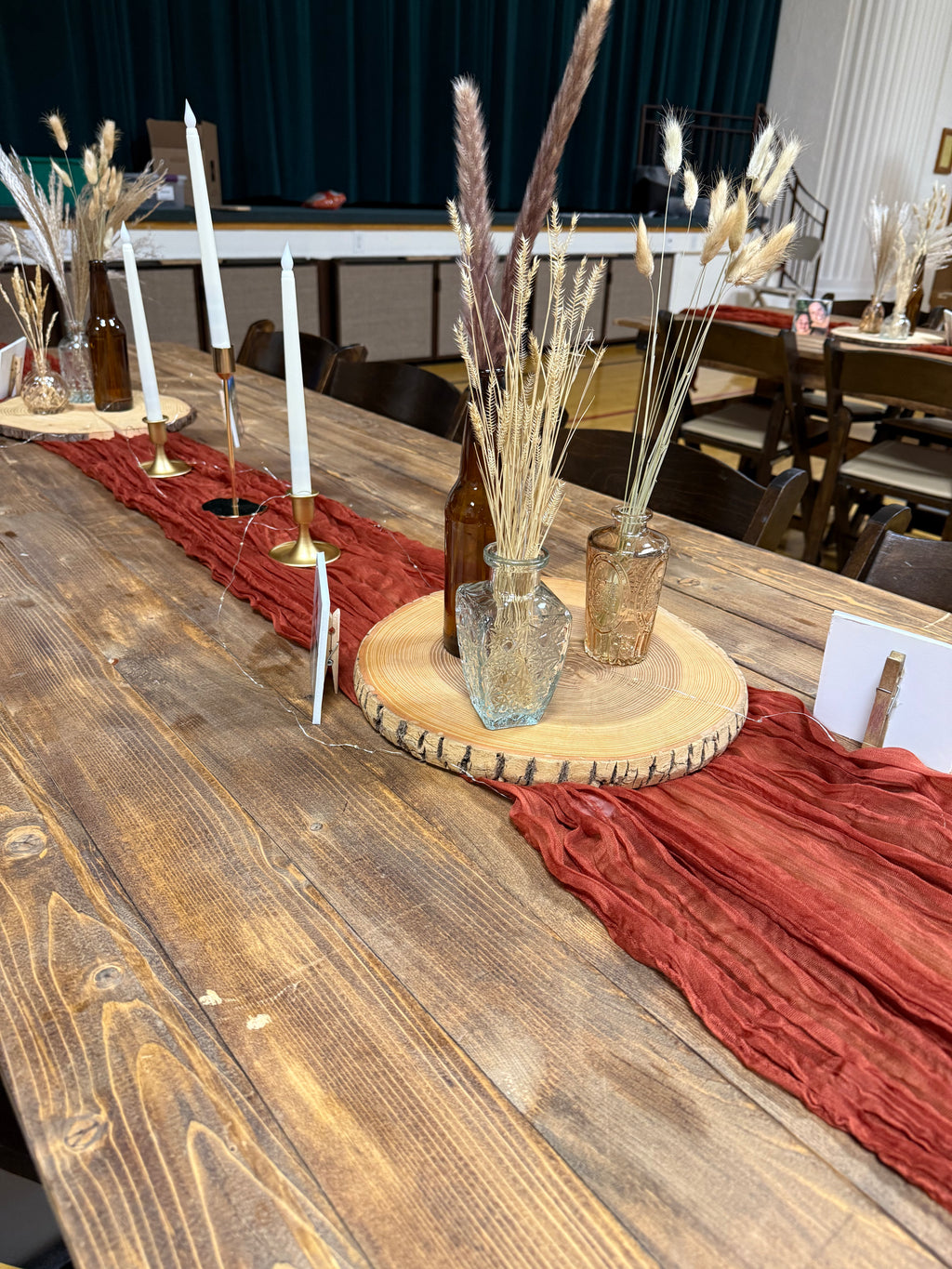 Decorative table setting with candles, bottles, and red runner on a wooden table.