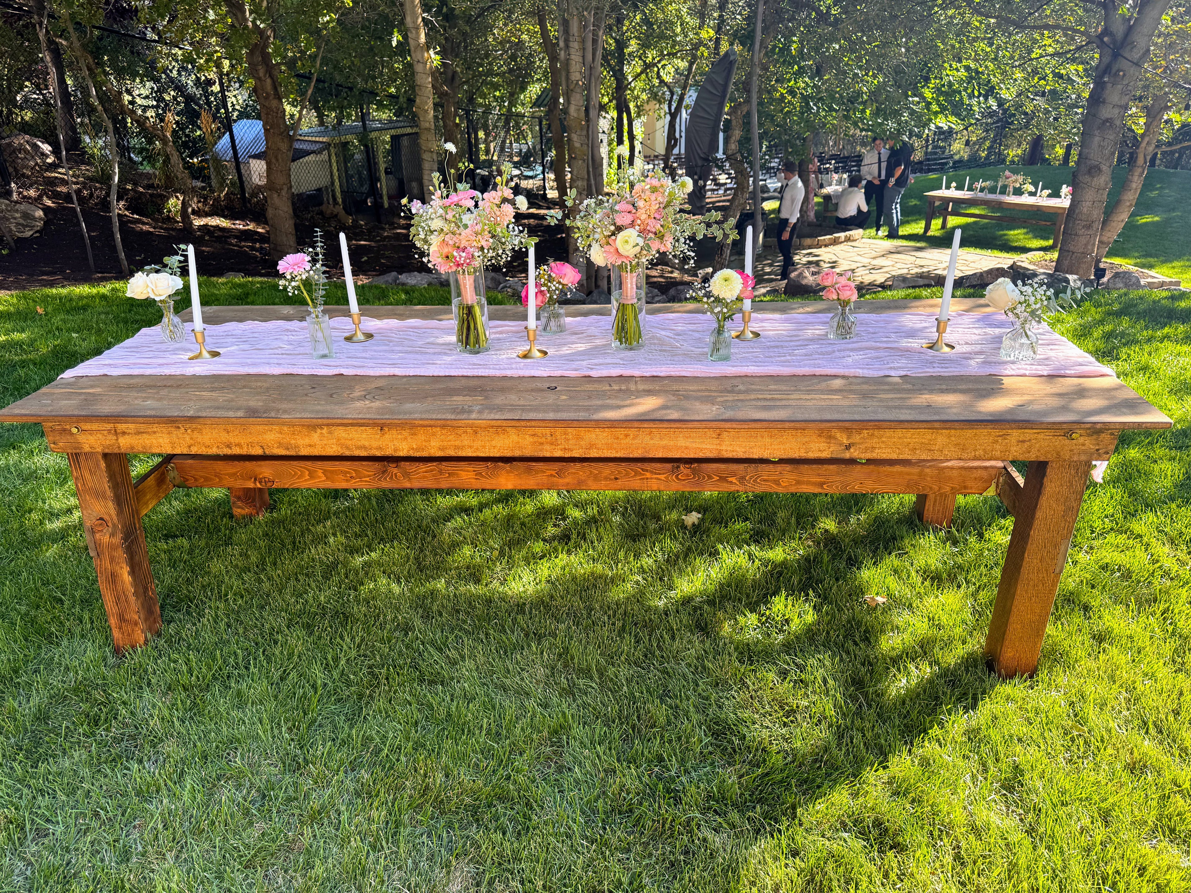 Long wooden table set with floral arrangements and candles on a grassy outdoor area all available for rent in central Utah.
